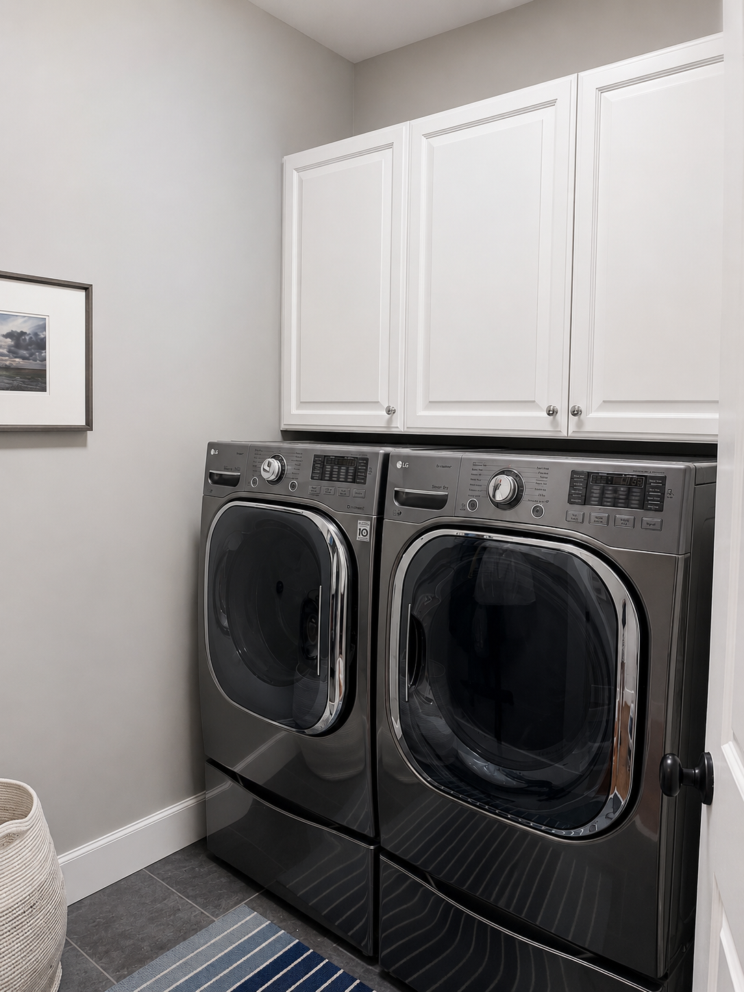 First-floor laundry room with side-by-side front-loading washer and dryer beneath white upper cabinets
