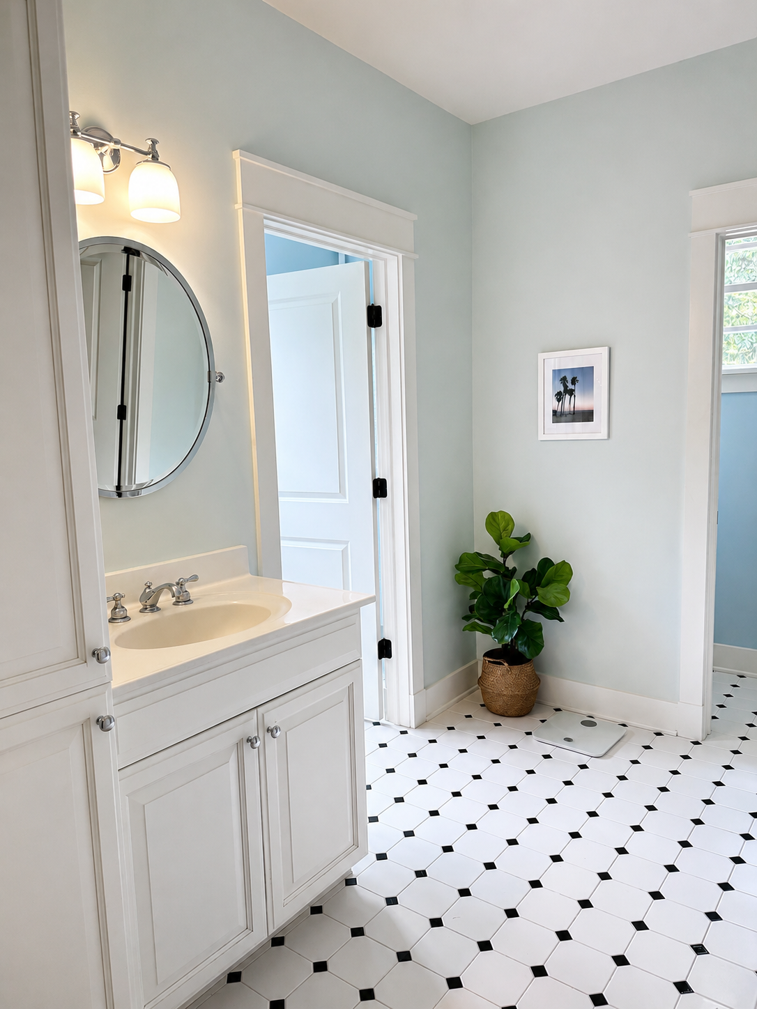 Mid-level bathroom with soft blue walls, white vanity, oval pivot mirror, and octagonal black-and-white tile floor
