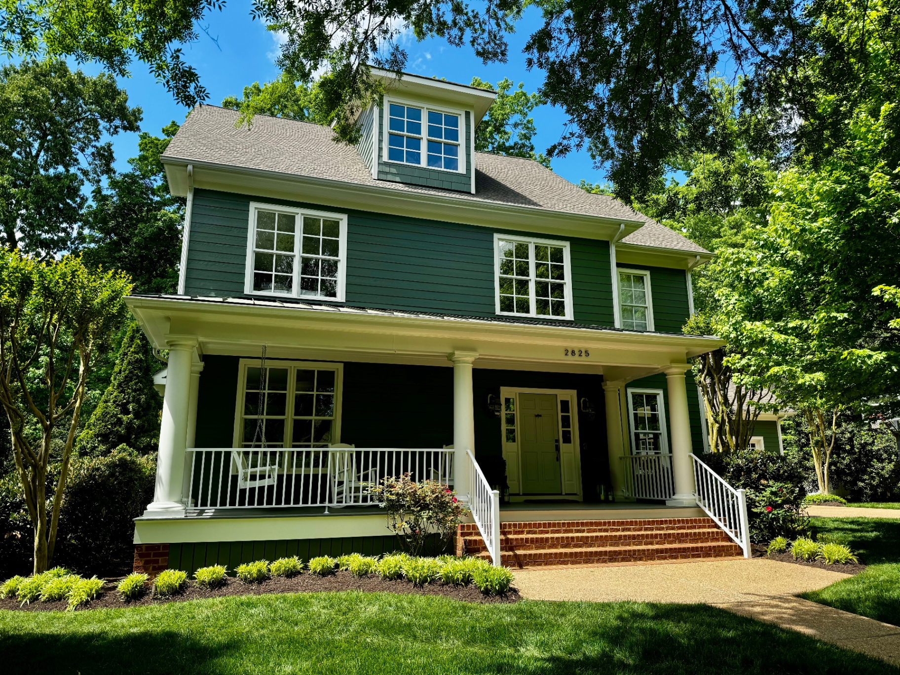 Daytime front view of 2825 Live Oak Lane with deep green siding, white columns, and wraparound porch