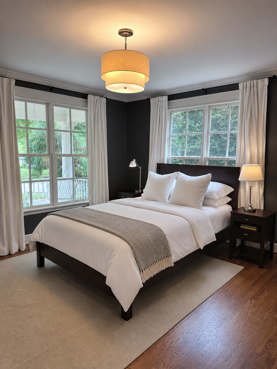 Primary bedroom with charcoal walls, dark wood bed, and tall windows overlooking the front porch