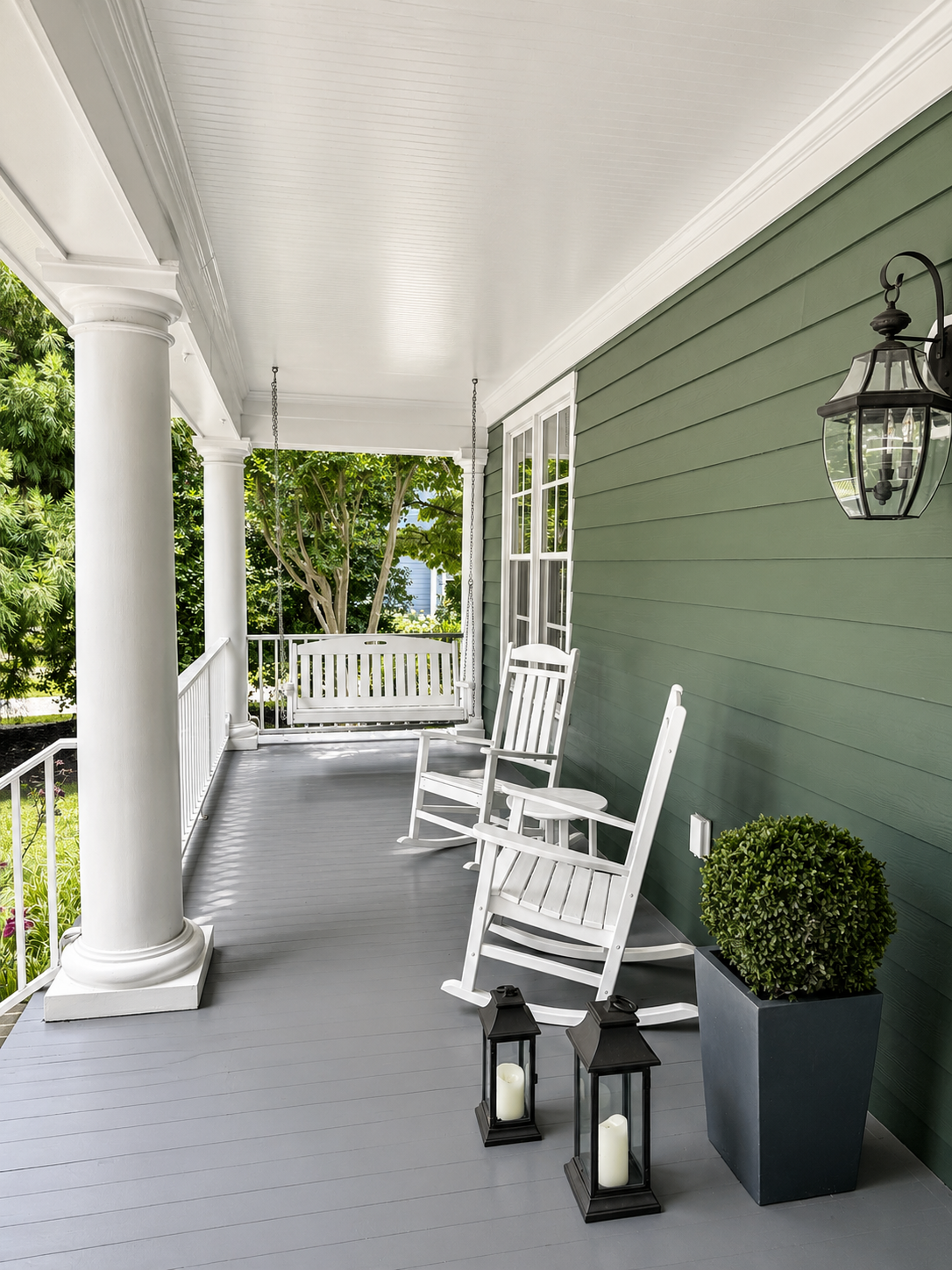 Front porch with white rocking chairs, hanging porch swing, and deep green siding